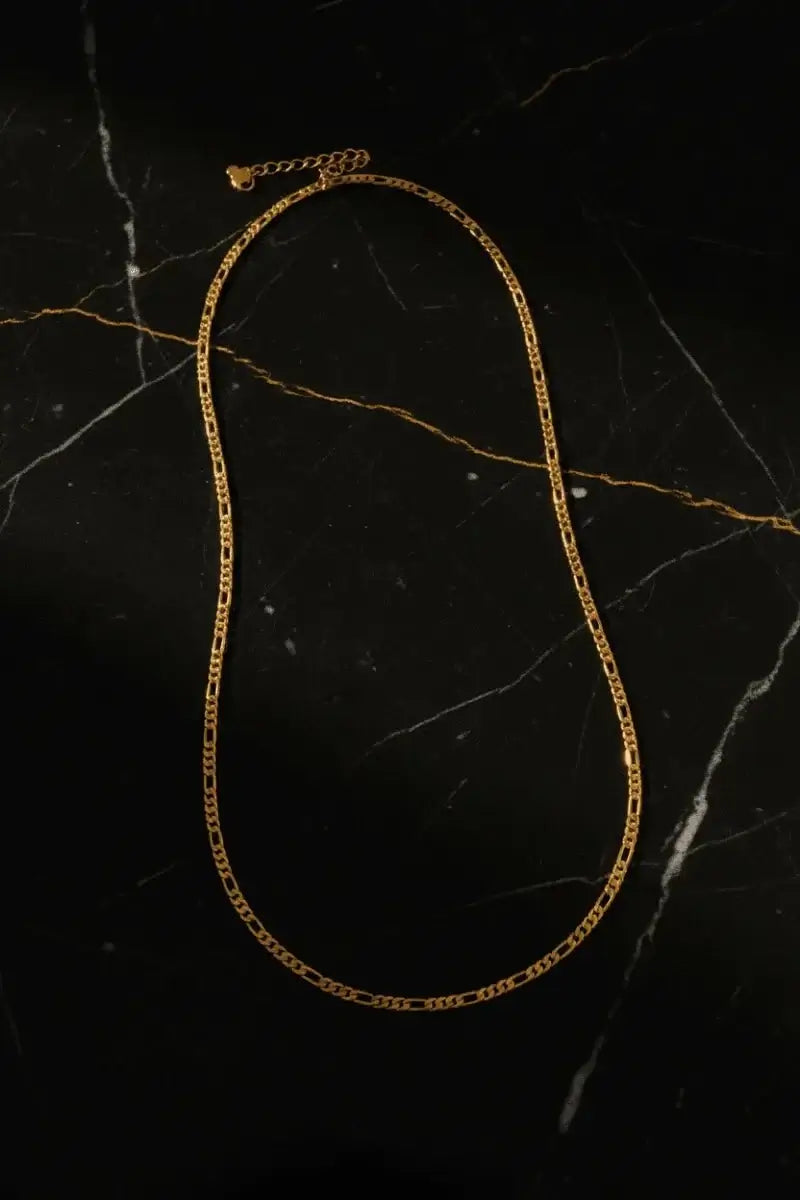 18kt gold titanium steel Figaro link chain on a black marble background, showcasing its elegant design.