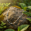 Anklet on rock with greenery, lizard and water droplets