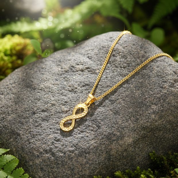 Complete gold infinity necklace on rock with greenery