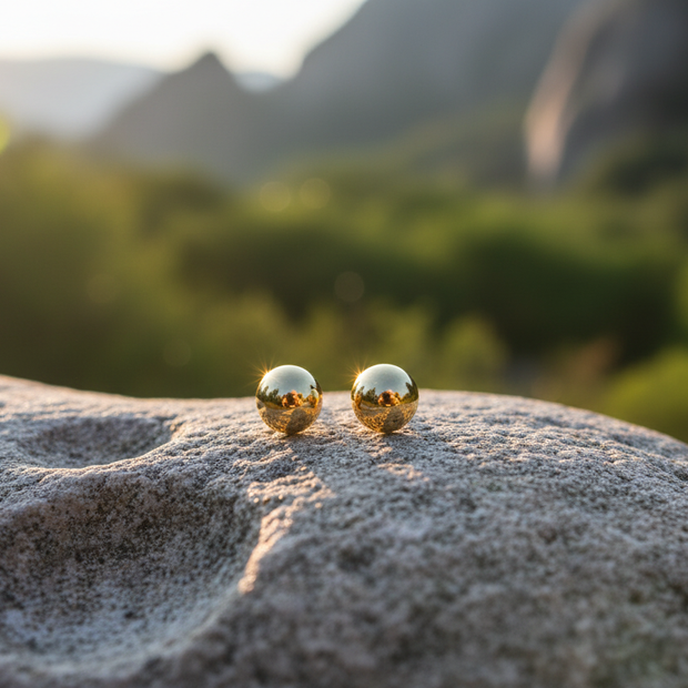Gold ball earrings on rock with natural sunlight