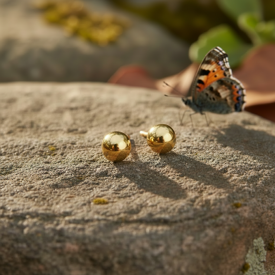 Gold ball earrings with butterfly on background rock