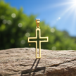 Gold cross pendant on rock with natural sunlight