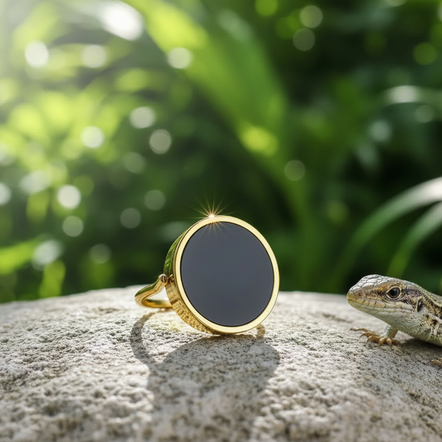 Gold ring with black onyx on rock with lizard and green background