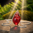 Red spiral shell charm close-up with silver snake chain on rock in sunlight