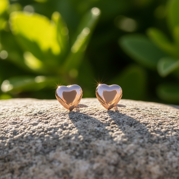 Rose gold heart stud earrings on rock with green background
