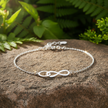 Silver infinity bracelet with sunlight sparkle on rock