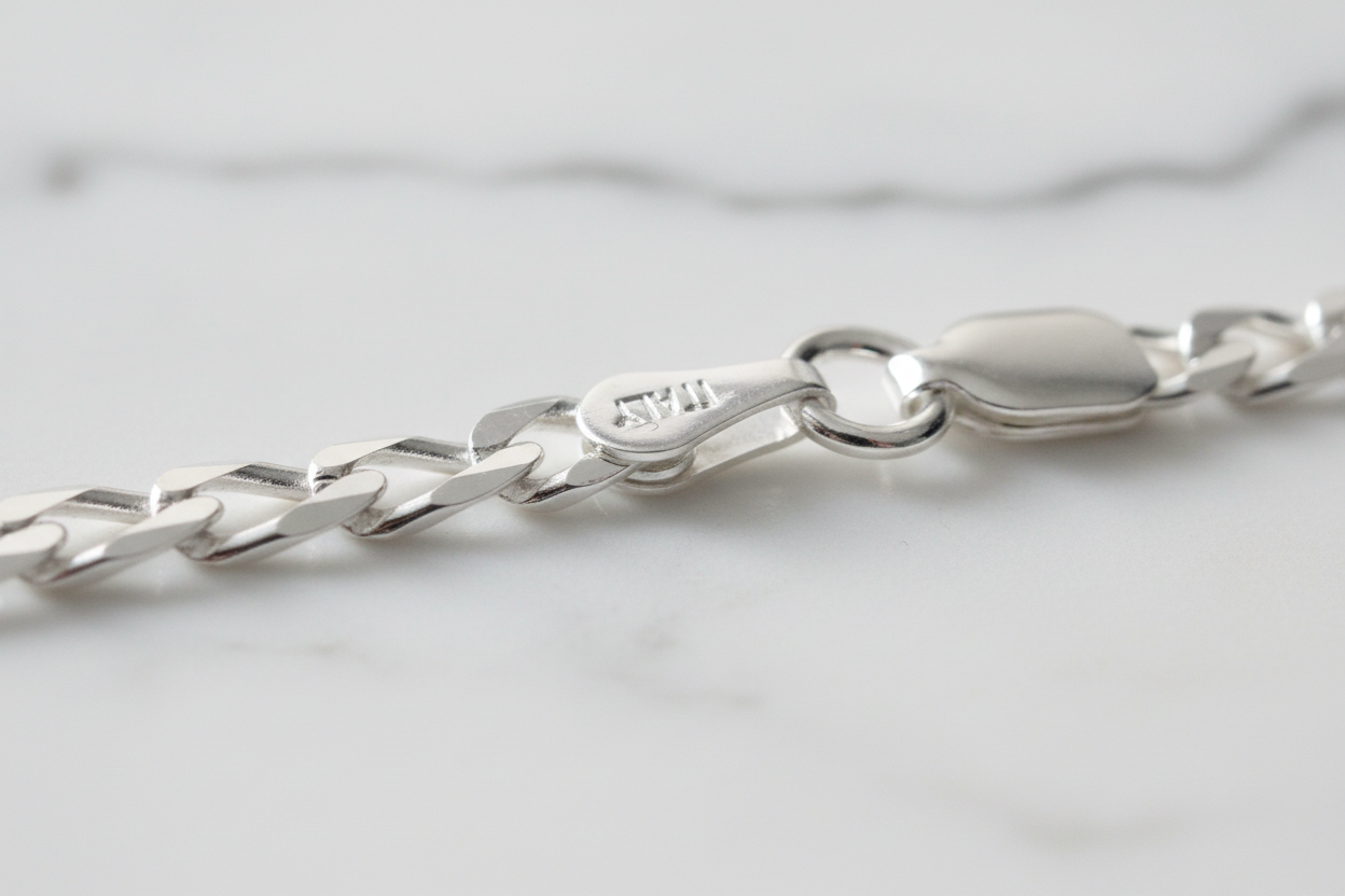 Sterling silver figaro chain bracelet clasp detail on natural stone background