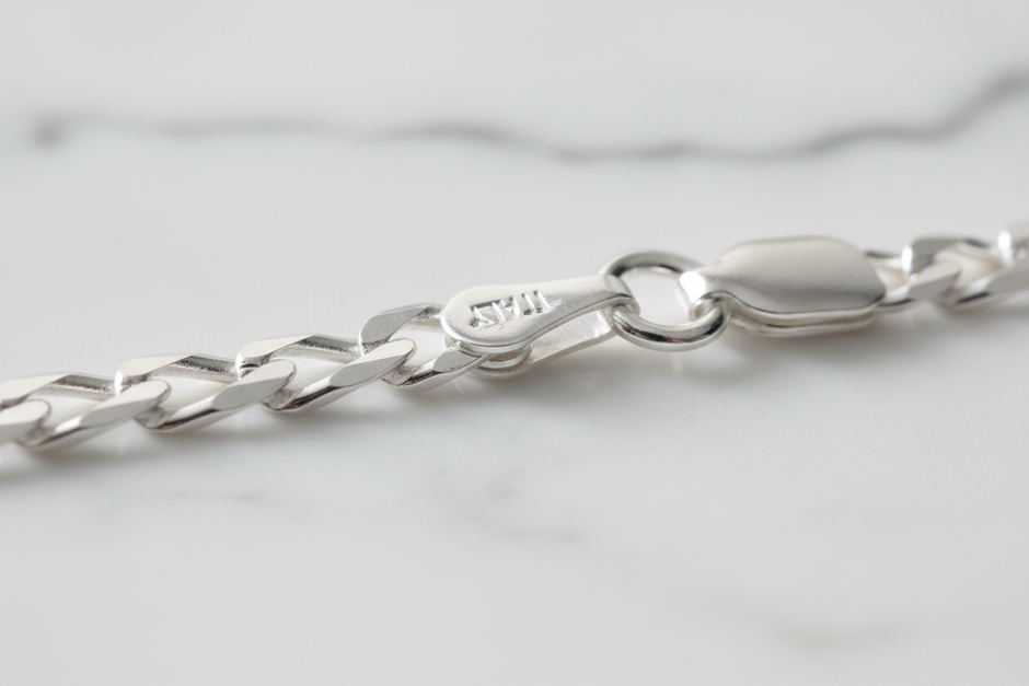 Sterling silver figaro chain bracelet clasp detail on natural stone background