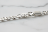 Sterling silver figaro chain bracelet clasp detail on natural stone background