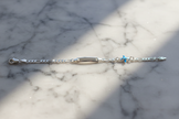 Sterling silver figaro chain bracelet displayed horizontally on natural stone with sparkle