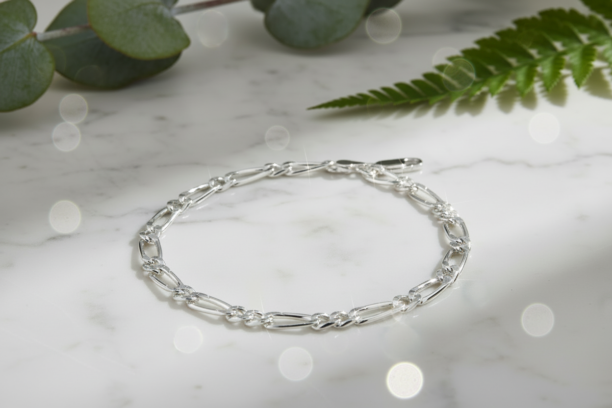 Sterling silver figaro chain bracelet in natural position on marble with sparkle