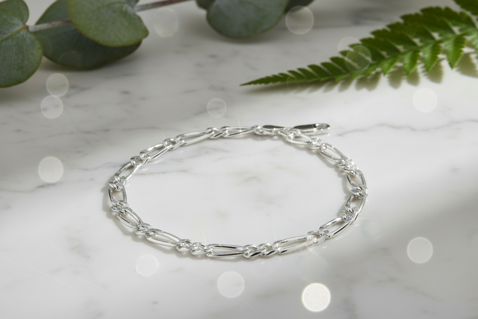 Sterling silver figaro chain bracelet in natural position on marble with sparkle