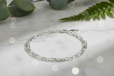 Sterling silver figaro chain bracelet in natural position on marble with sparkle